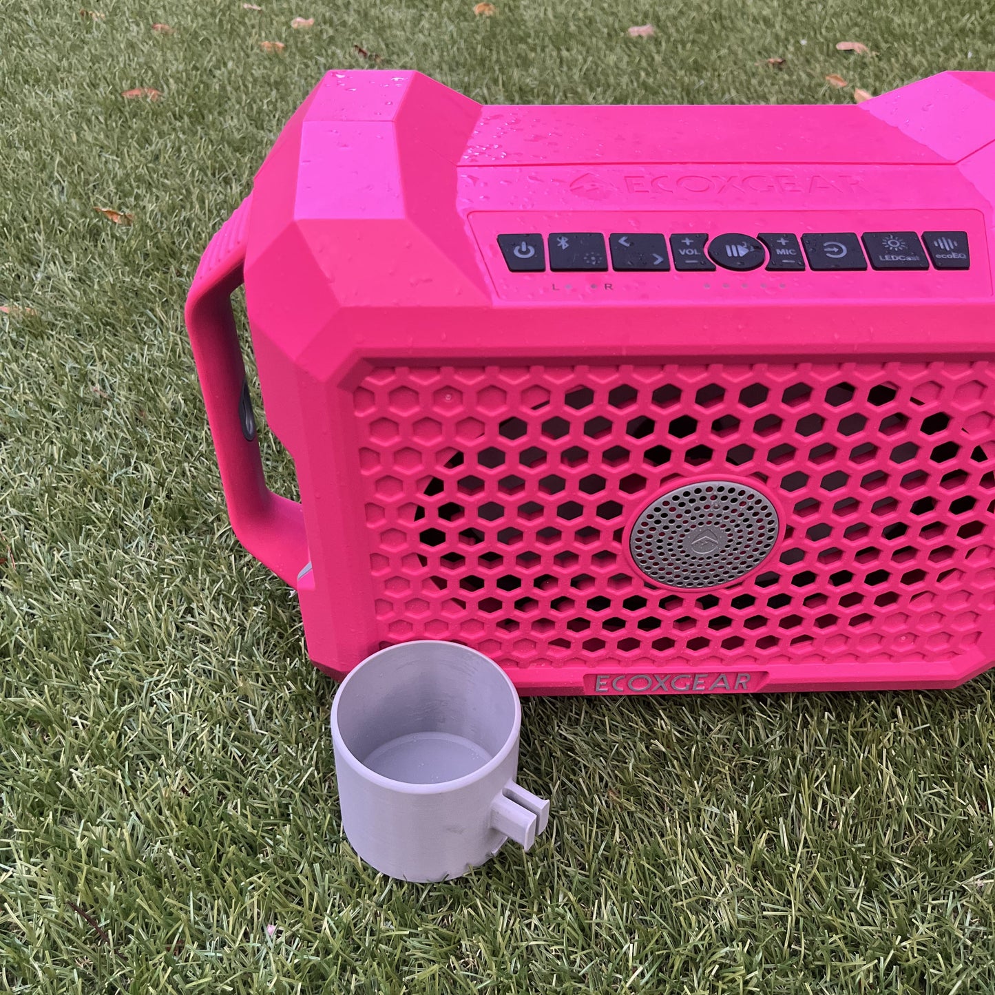 Pink ECOXGEAR Defender speaker shown with 12oz Can Holder attachment from Ruckus Marine, highlighting the clip mechanism