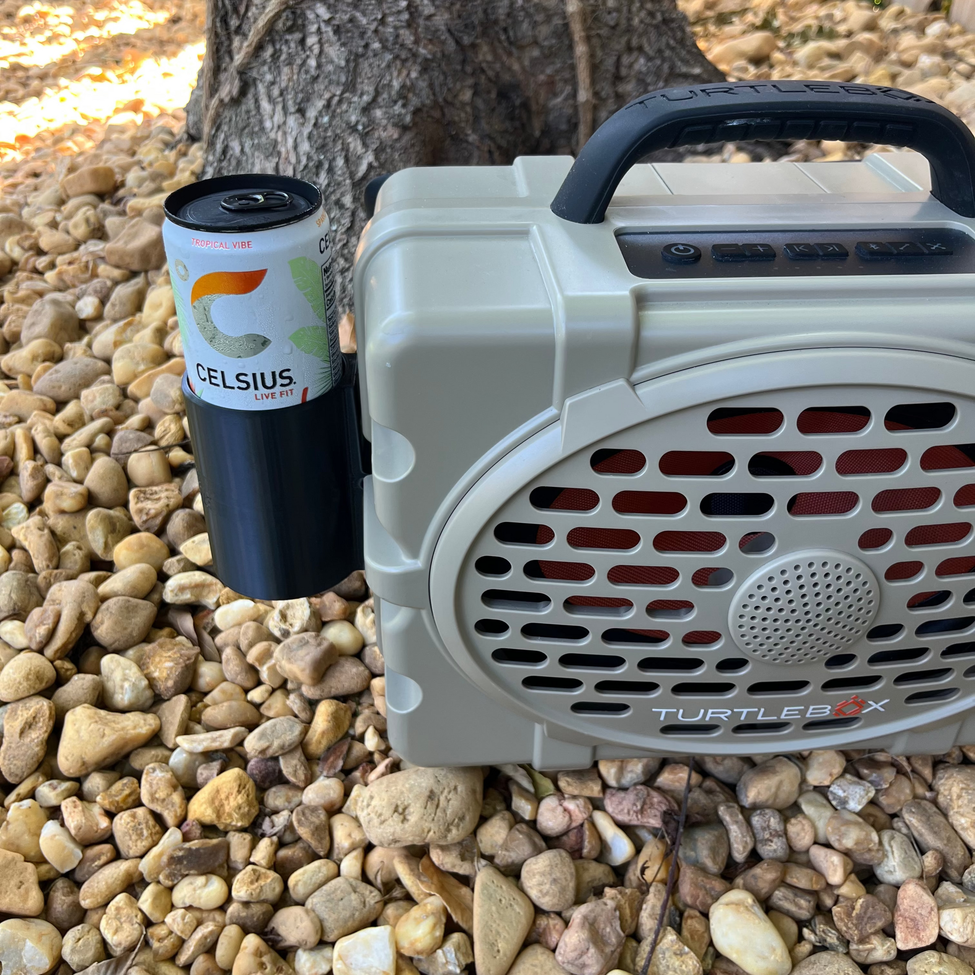 Turtlebox Slim Can Attachment shown in black with a Celcius energy drink on a bed of rocks