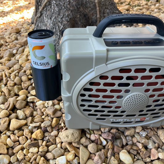 Turtlebox Slim Can Attachment shown in black with a Celcius energy drink on a bed of rocks