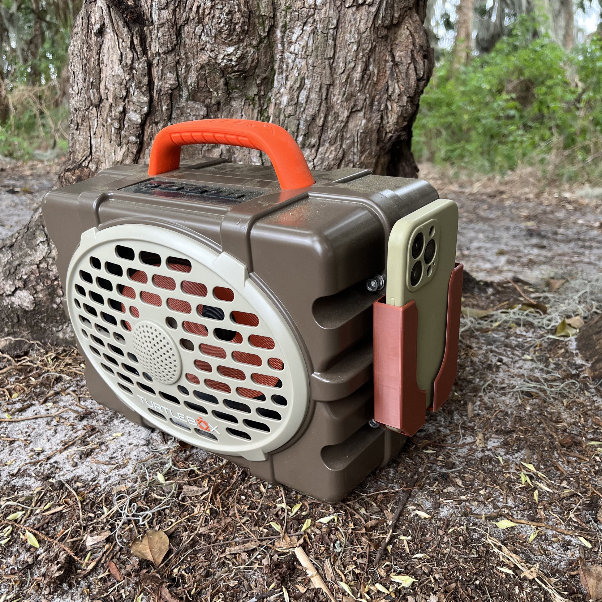 A brown Turtlebox Phone holder from Ruckus Marine holding an iPhone in the woods.